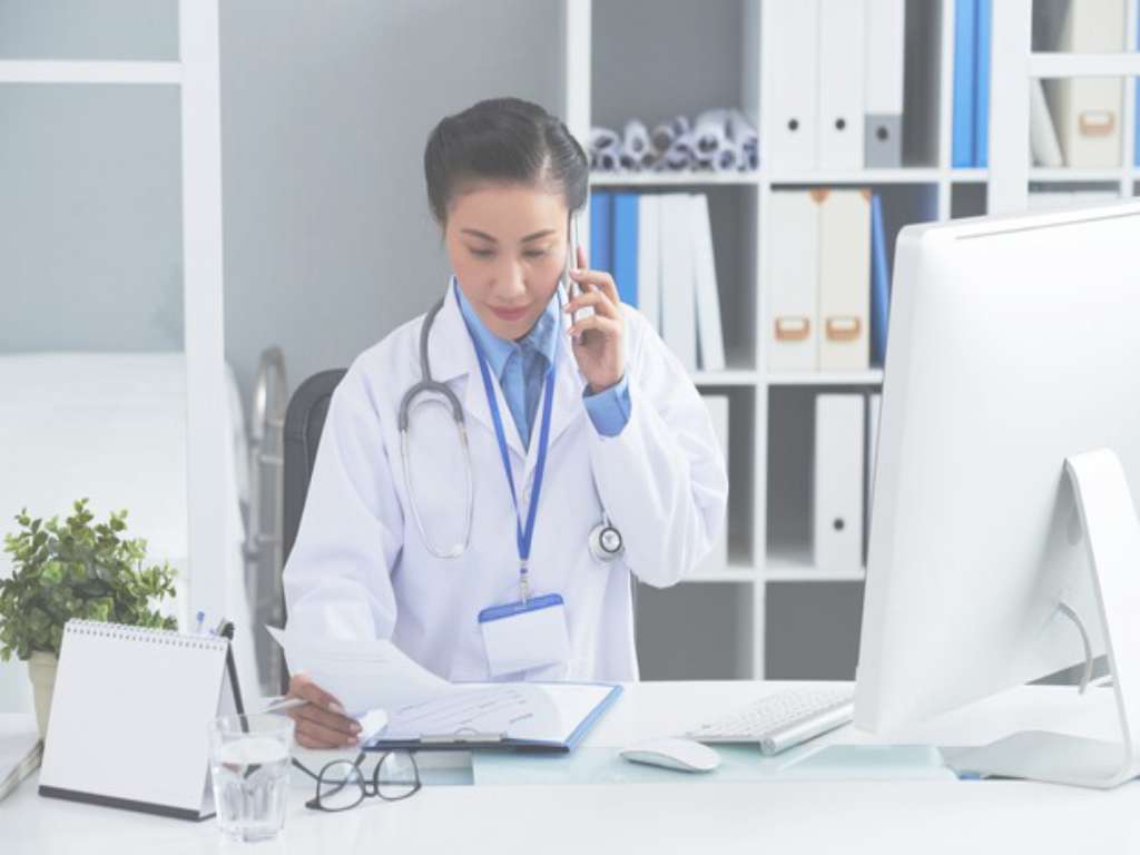 asian female doctor sitting desk office calling mobile phone